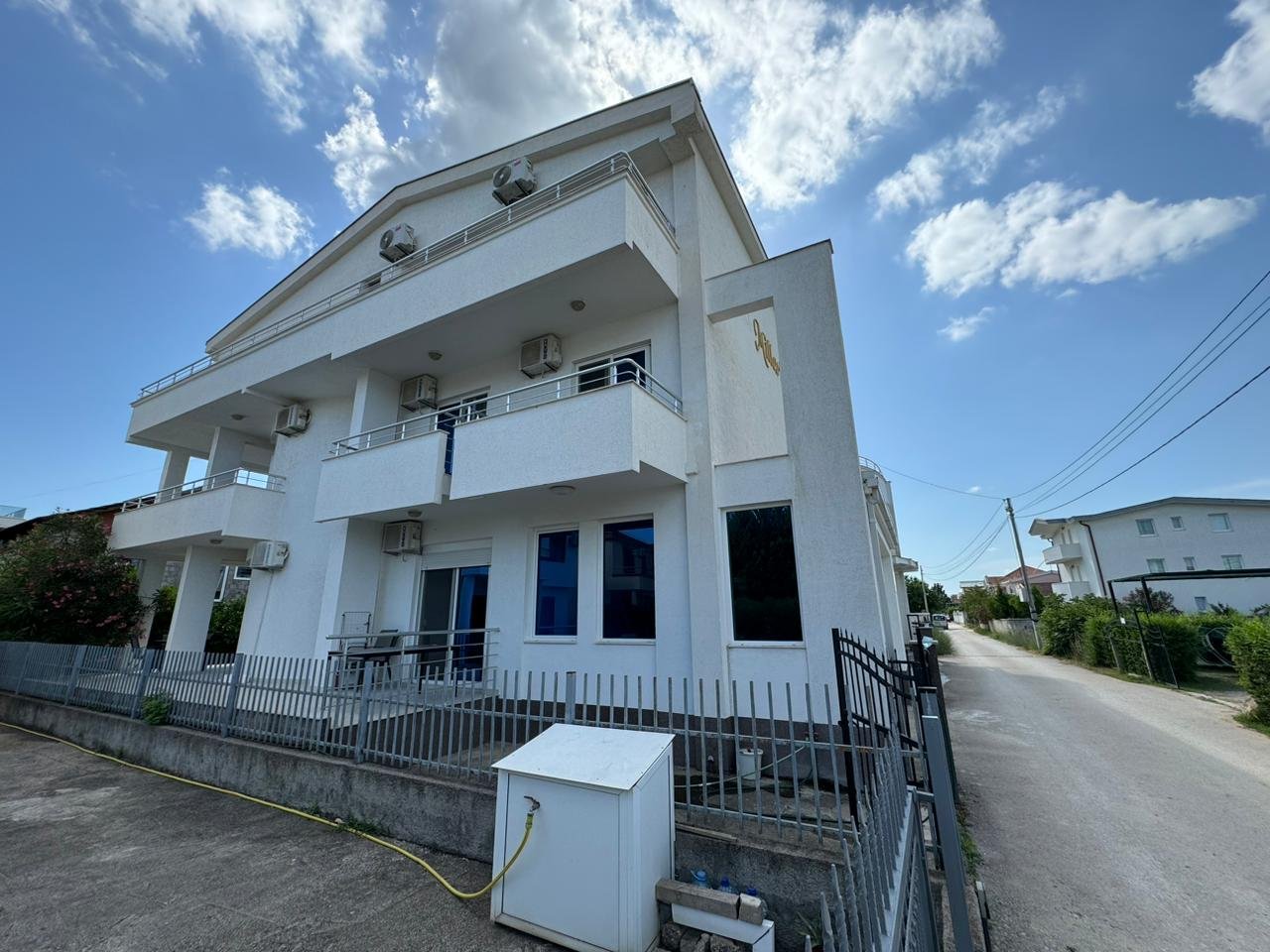 Modern white two-story home with balconies, fenced yard, and paved driveway in Ulcinj. Exclusive on immorenta.me by Ekosphere doo.