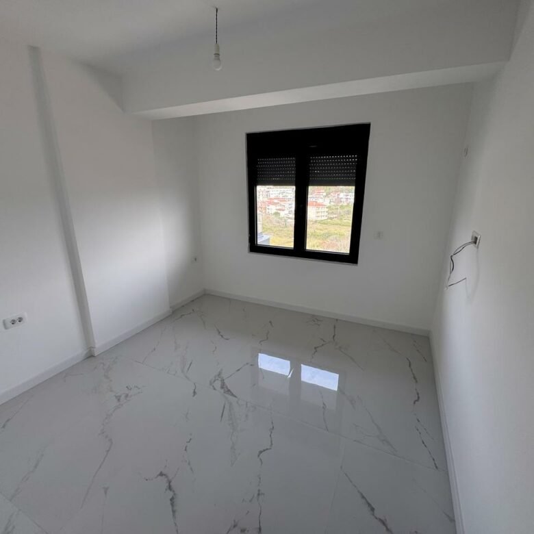 Modern minimalist room in Ulcinj with white walls, elegant tile floors, and a black-framed window. Offered by immorenta.me.