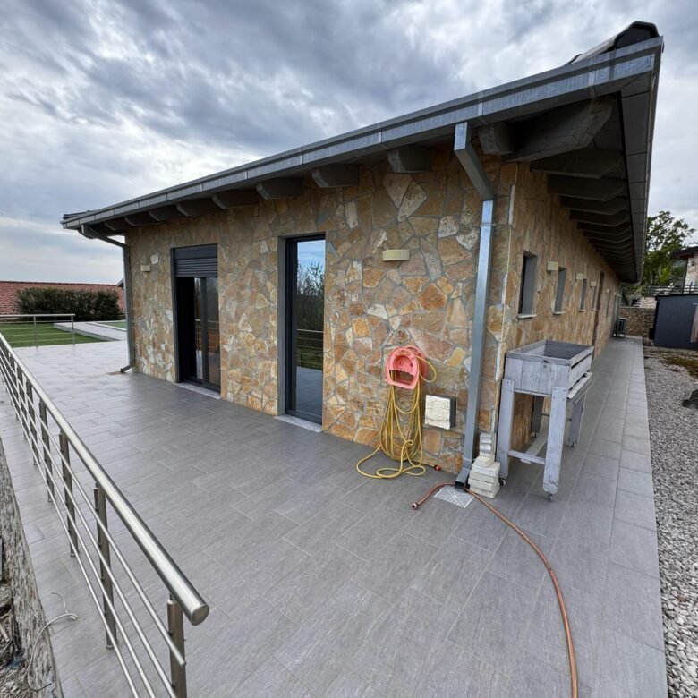 Elegant stone-clad home with spacious gray-tiled patio, glass doors, and modern railings&mdash;prime Ulcinj investment by ekosphere doo.