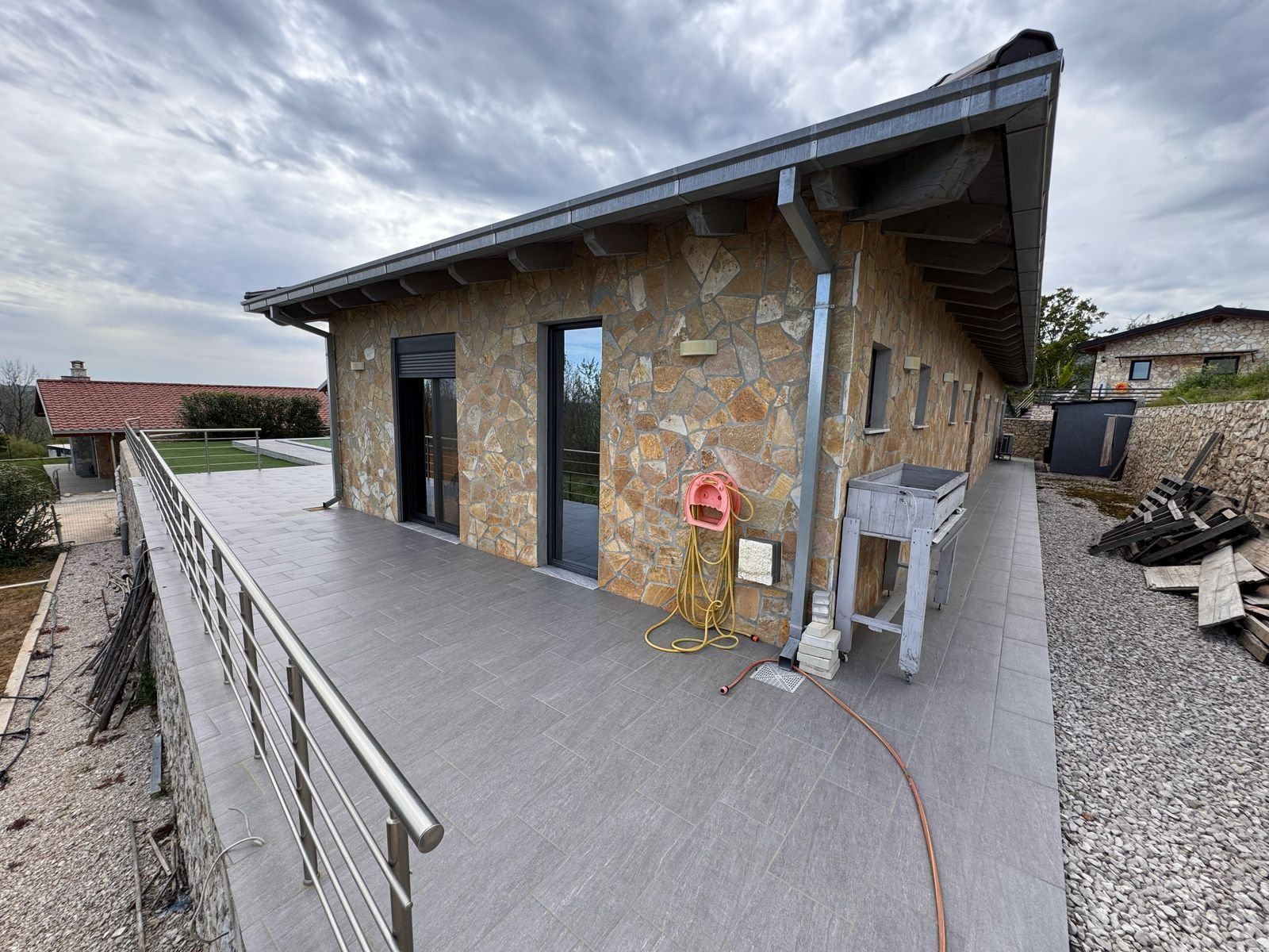 Elegant stone-clad home with spacious gray-tiled patio, glass doors, and modern railings&mdash;prime Ulcinj investment by ekosphere doo.