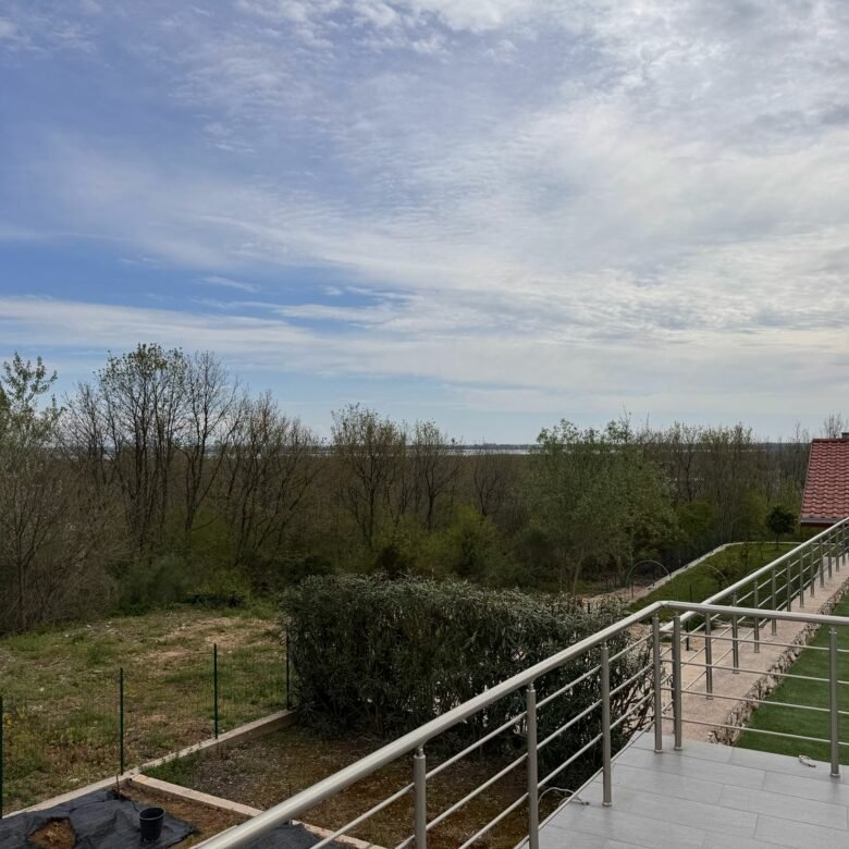 Spacious tiled balcony with metal railing, lush lawn, and red-roofed house in Ulcinj, Montenegro&mdash;exclusive on immorenta.me by ekosphere doo.