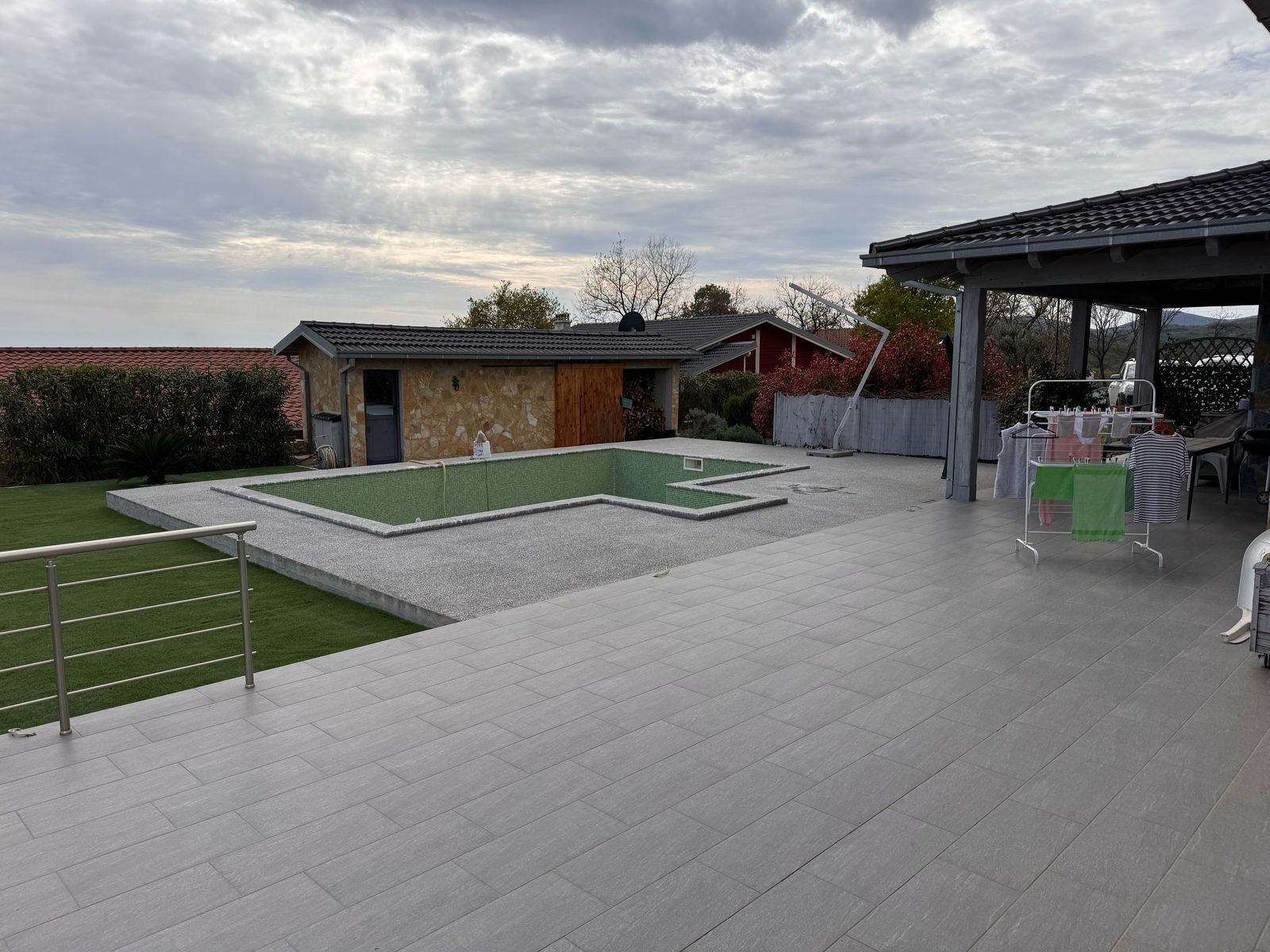Spacious patio with gray tiles, empty rectangular pool, shed, green lawn&mdash;premium Ulcinj Montenegro property by ekosphere doo.