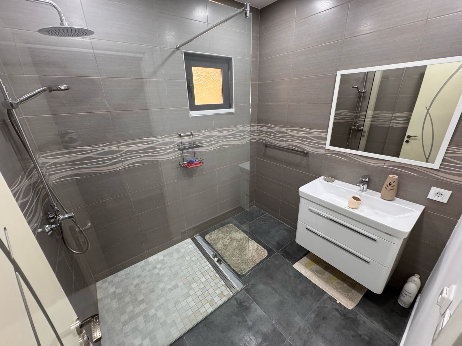 Stylish Ulcinj bathroom: gray tiles, walk-in shower, rainfall heads, vanity, mirror&mdash;premium real estate by immorenta.me.