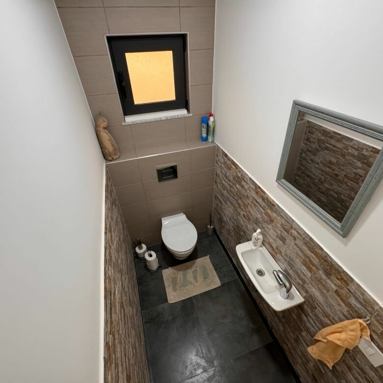 Modern small bathroom in Ulcinj property, with toilet, wall sink, mirror, and window. Invest via immorenta.me by ekosphere doo.