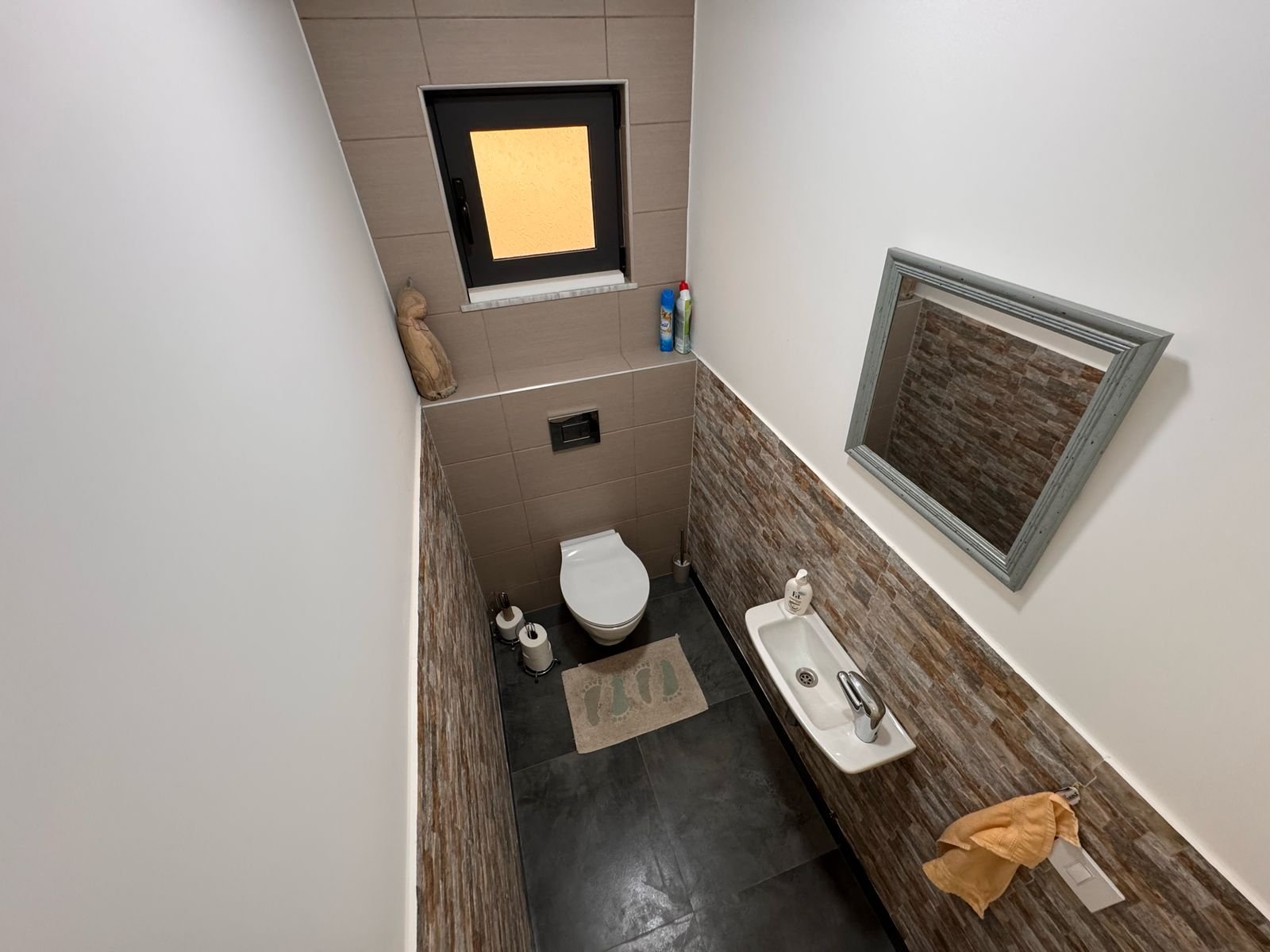 Modern small bathroom in Ulcinj property, with toilet, wall sink, mirror, and window. Invest via immorenta.me by ekosphere doo.