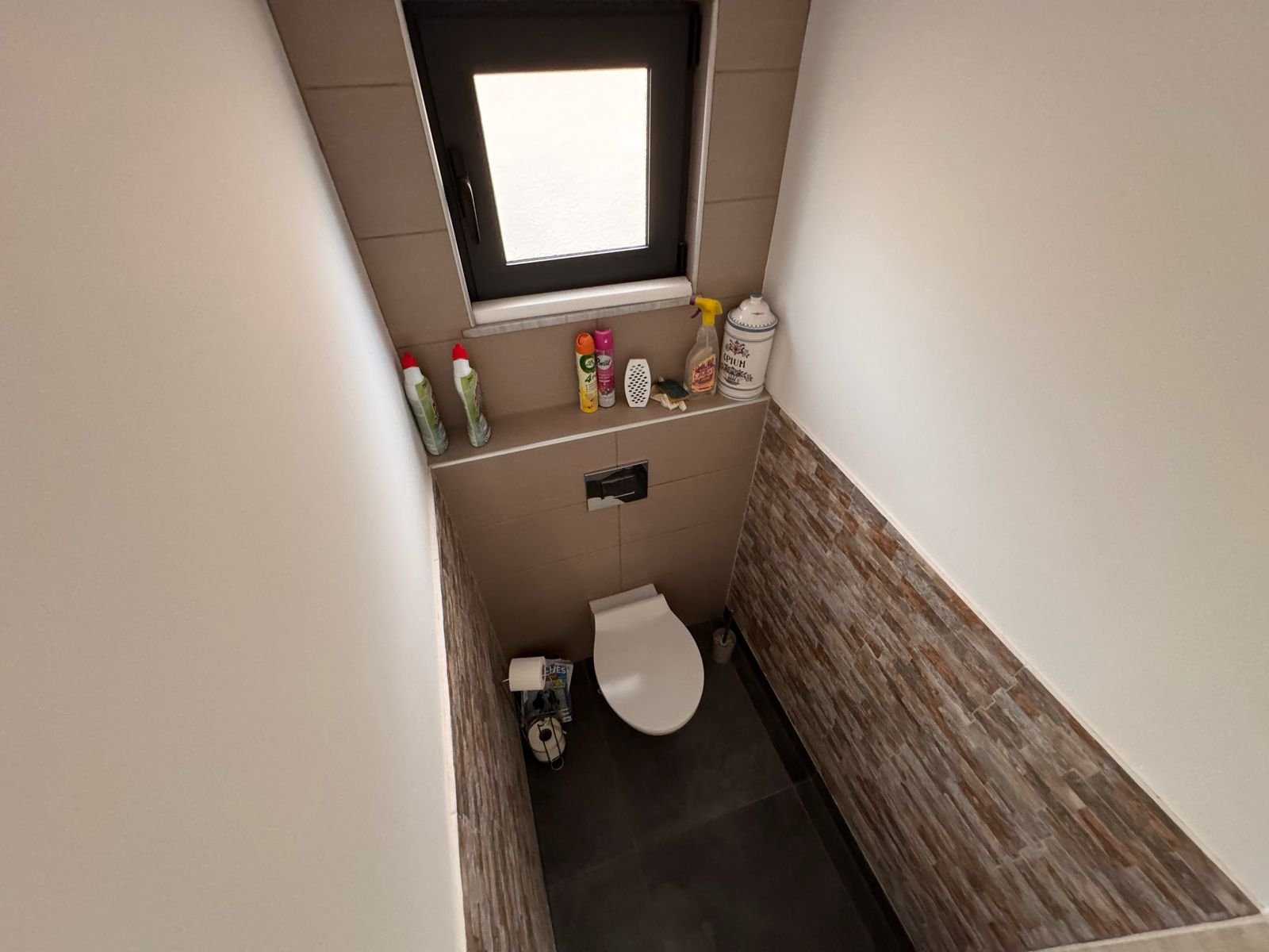 Modern small bathroom in Ulcinj with wall-mounted toilet, eco-friendly brown tiles, and window. Featured on immorenta.me by ekosphere doo.
