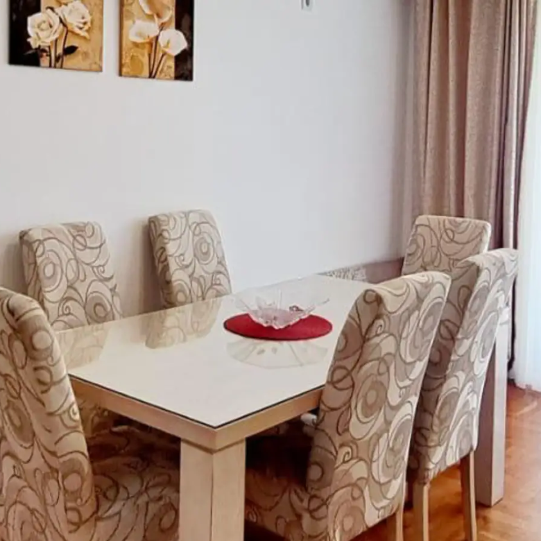Elegant Ulcinj Montenegro property dining area with glass-top table, designer chairs, sheer curtains, floral art. Eksphere doo project.