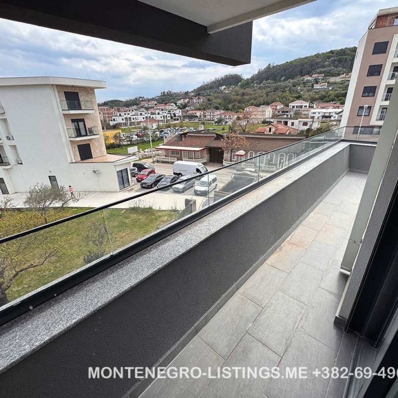 Stunning balcony view with glass railing over prime Ulcinj real estate&mdash;buildings, cars, lush hills. immorenta.me by Ekosphere doo.