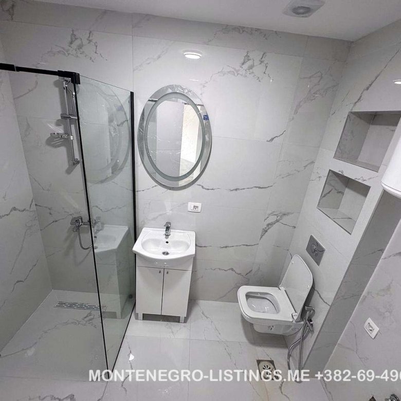 Elegant Ulcinj bathroom with marble tiles, glass shower, modern fixtures. Great real estate investment at immorenta.me by Ekosphere.