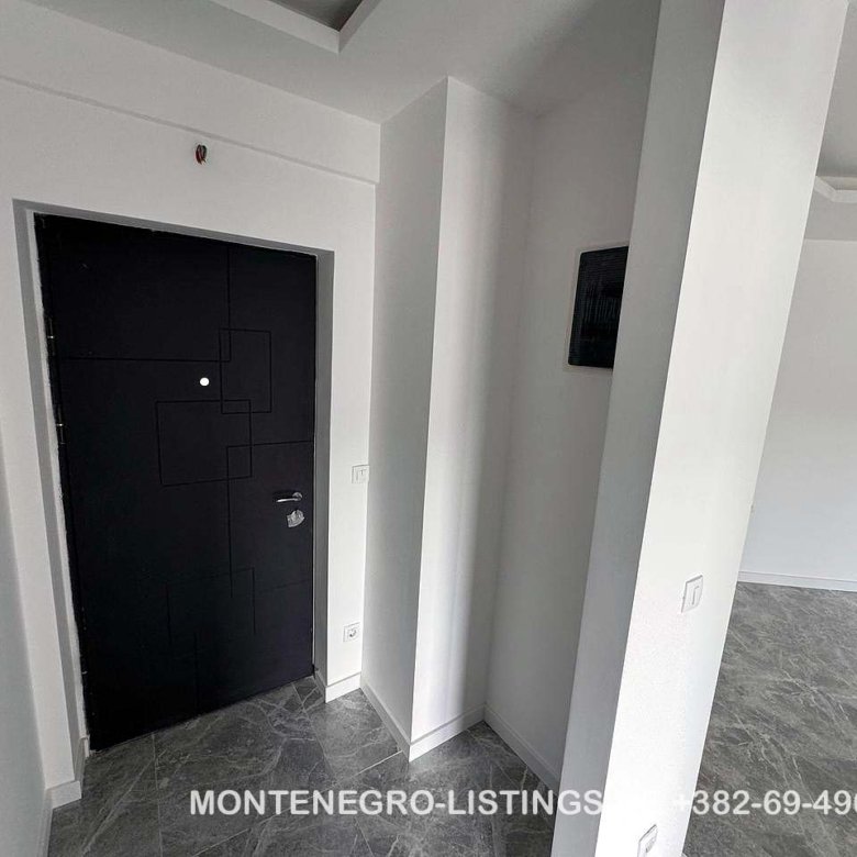 Contemporary Ulcinj apartment entry: sleek black door, white walls, grey tiled floor. Invest with immorenta.me by ekosphere doo.