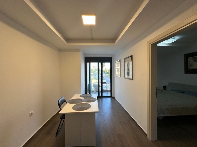 Modern minimalist dining area with sleek white table, balcony access, quality wood floors&mdash;ideal Ulcinj real estate at immorenta.me (a project of ekosphere doo).