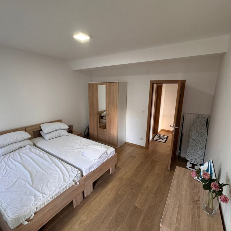 Discover a stylish Ulcinj bedroom with twin beds, mirrored wardrobe, dresser, and ironing board&mdash;prime real estate by Ekosphere DOO.