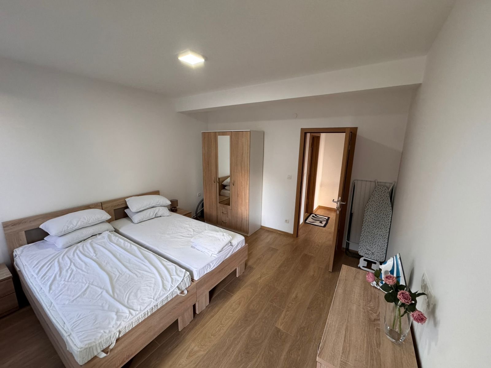 Discover a stylish Ulcinj bedroom with twin beds, mirrored wardrobe, dresser, and ironing board&mdash;prime real estate by Ekosphere DOO.