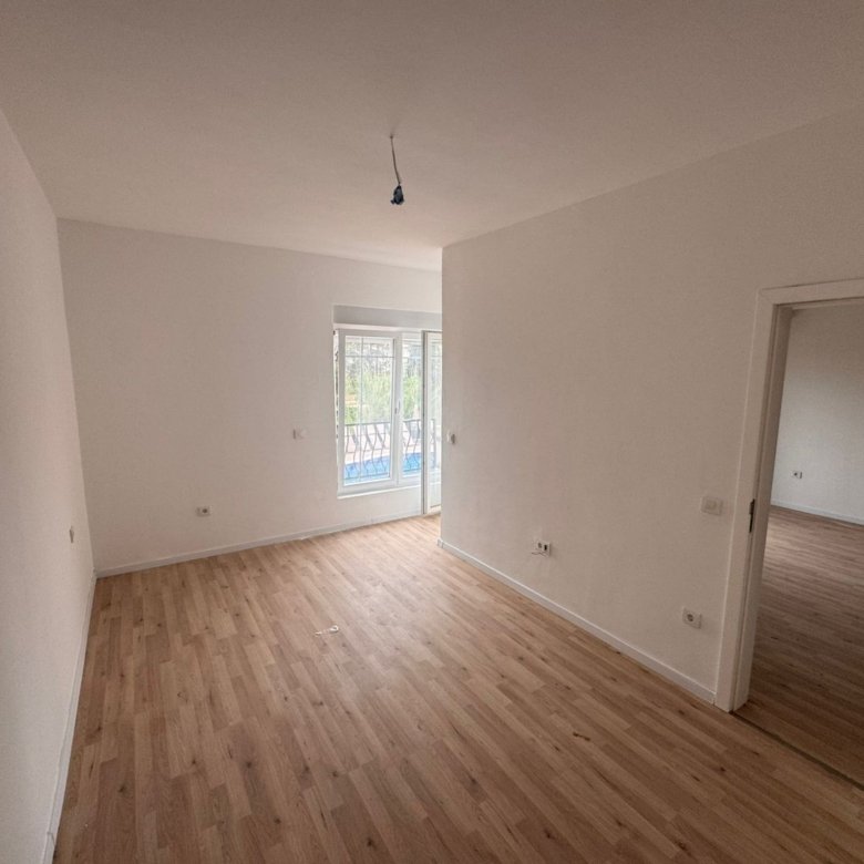 Bright empty room in Ulcinj with wood floors, balcony access, and white walls&mdash;a prime Montenegro real estate by Ekosphere on immorenta.me.