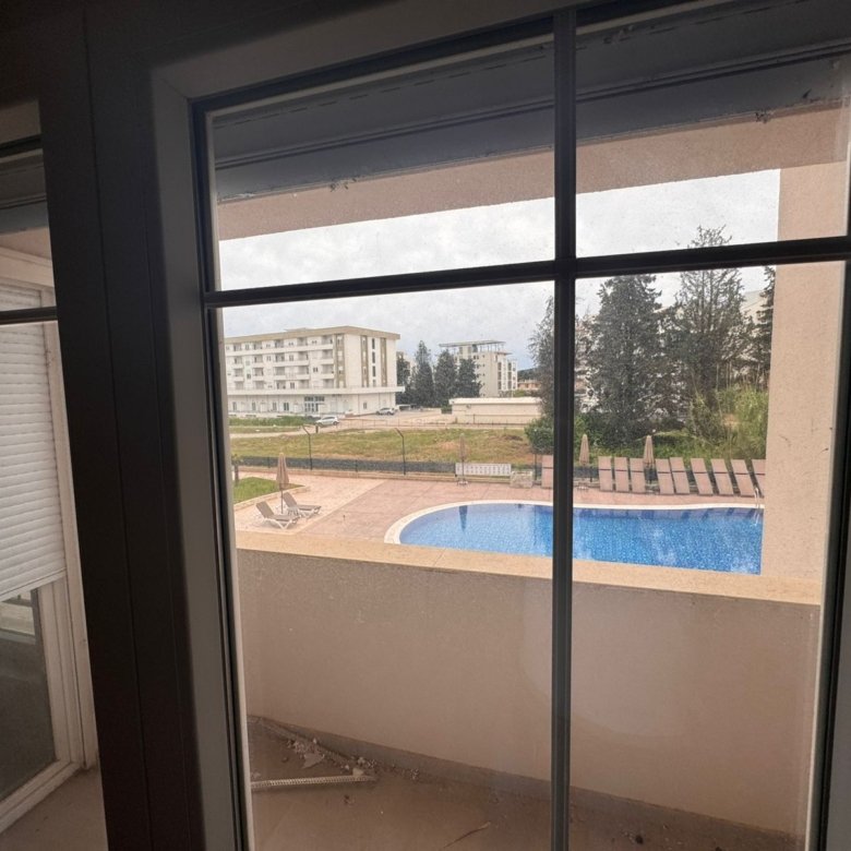 Bright glass doors open to a balcony with pool, loungers, and modern apartments&mdash;prime Ulcinj real estate by Ekosphere, immorenta.me.