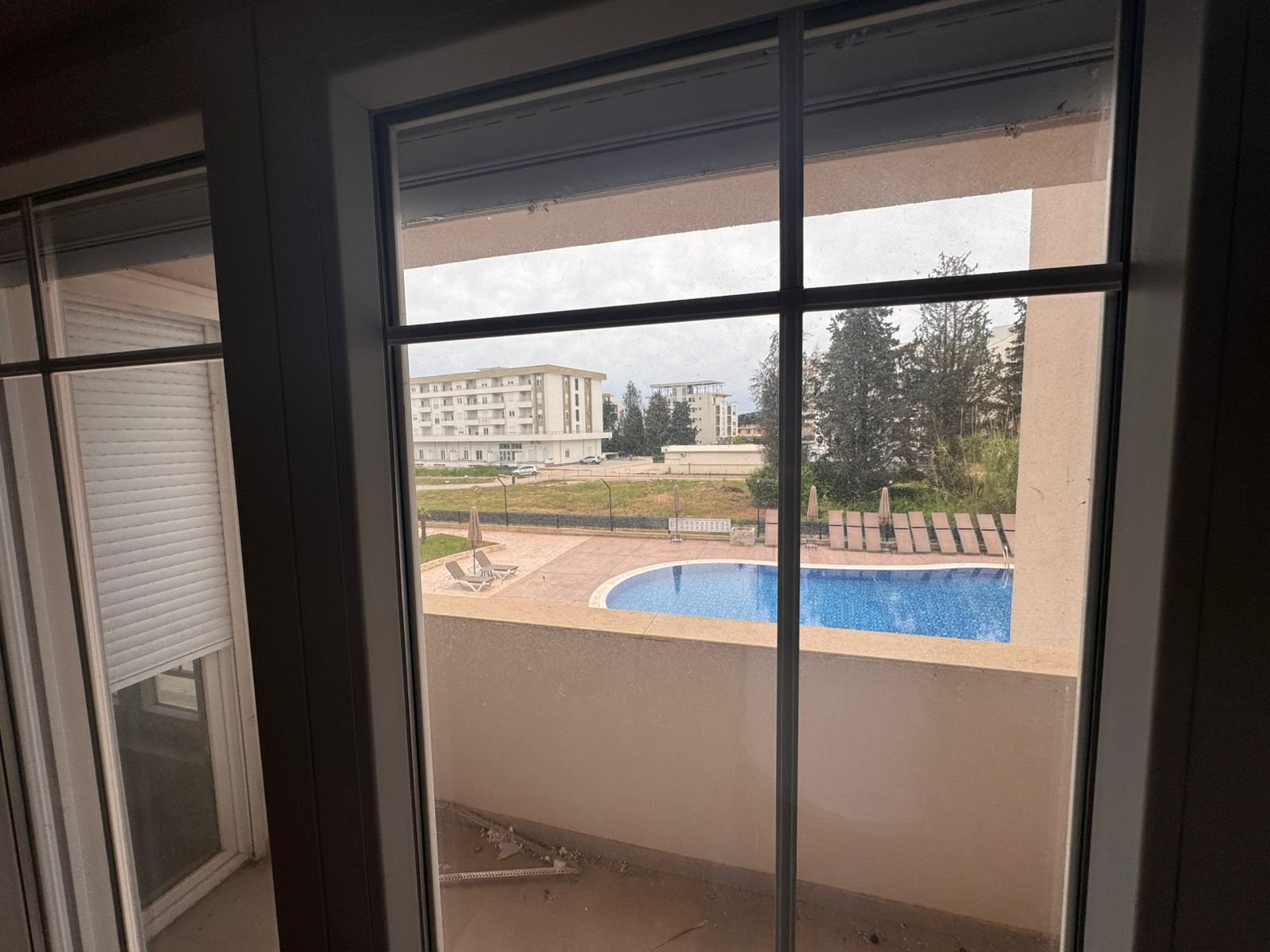 Bright glass doors open to a balcony with pool, loungers, and modern apartments&mdash;prime Ulcinj real estate by Ekosphere, immorenta.me.