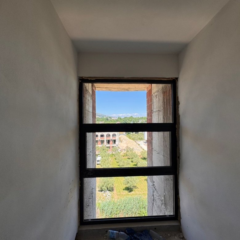 Bright window view reveals lush greenery, Ulcinj properties, mountain vistas&mdash;invest in Montenegro real estate via immorenta.me.