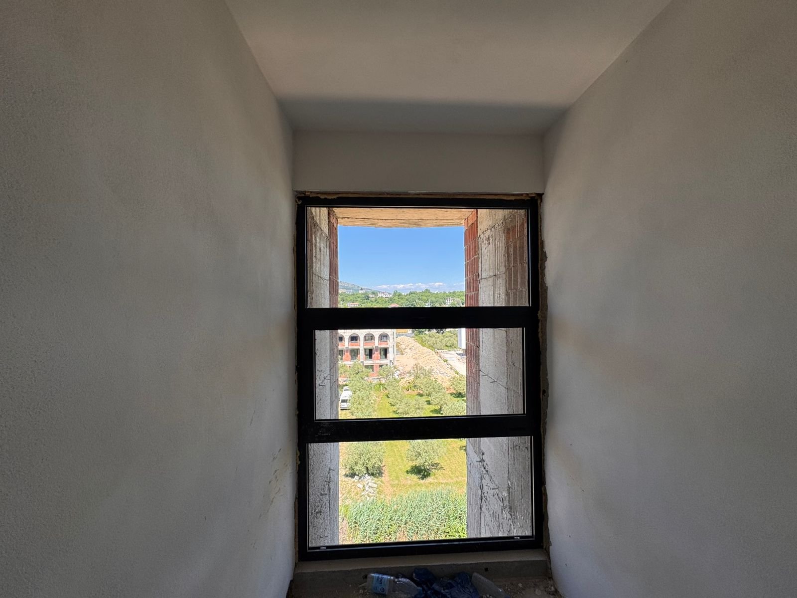 Bright window view reveals lush greenery, Ulcinj properties, mountain vistas&mdash;invest in Montenegro real estate via immorenta.me.