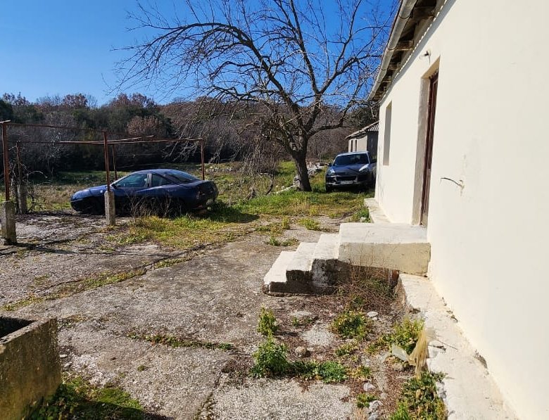 Bright concrete yard next to a pale building with steps, cars, and hills&mdash;prime Ulcinj real estate on immorenta.me by ekosphere doo.