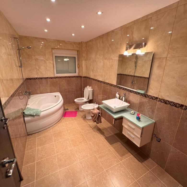 Modern bathroom in Ulcinj with beige tiles, corner tub, window, and quality fixtures&mdash;exclusive property at immorenta.me by ekosphere doo.