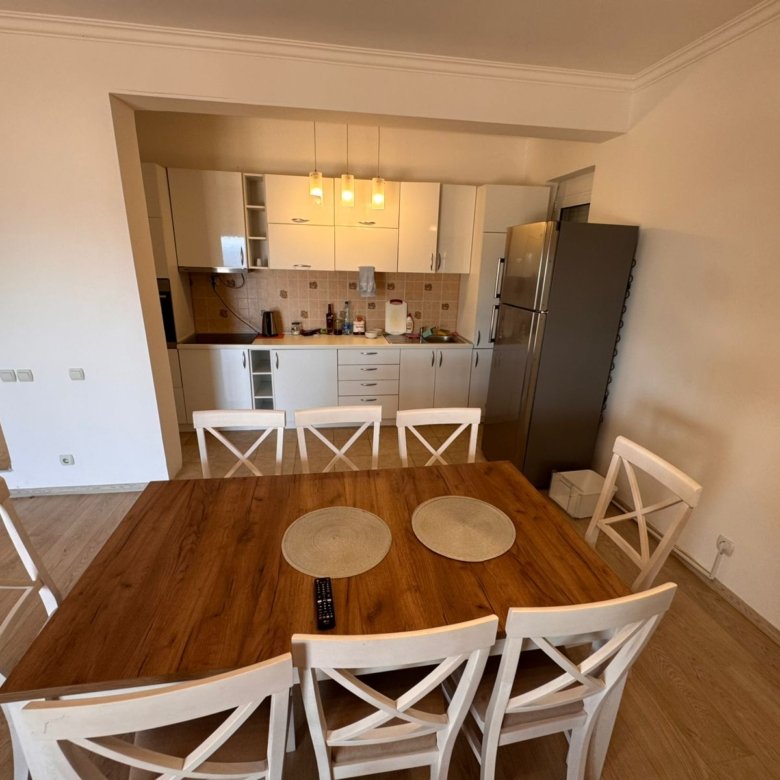 Modern Ulcinj kitchen with white cabinets, stainless fridge, wood table; ideal real estate on immorenta.me by ekosphere doo.