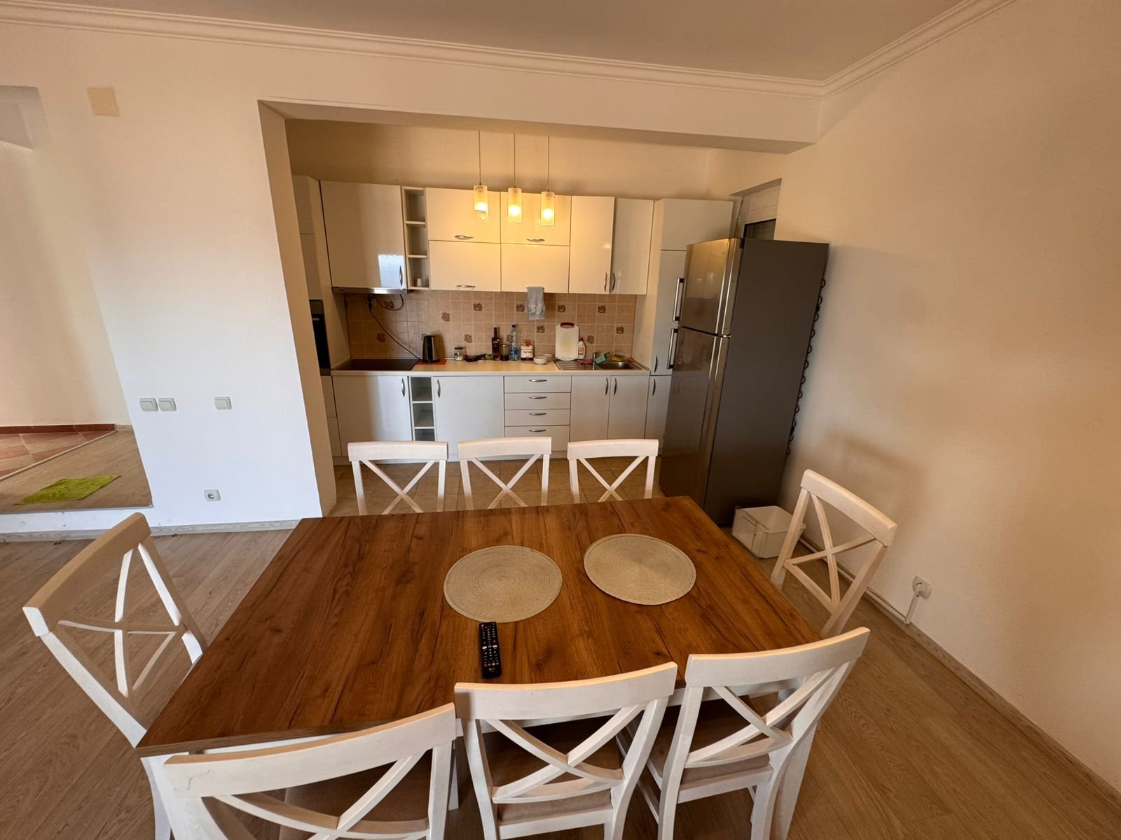 Modern Ulcinj kitchen with white cabinets, stainless fridge, wood table; ideal real estate on immorenta.me by ekosphere doo.