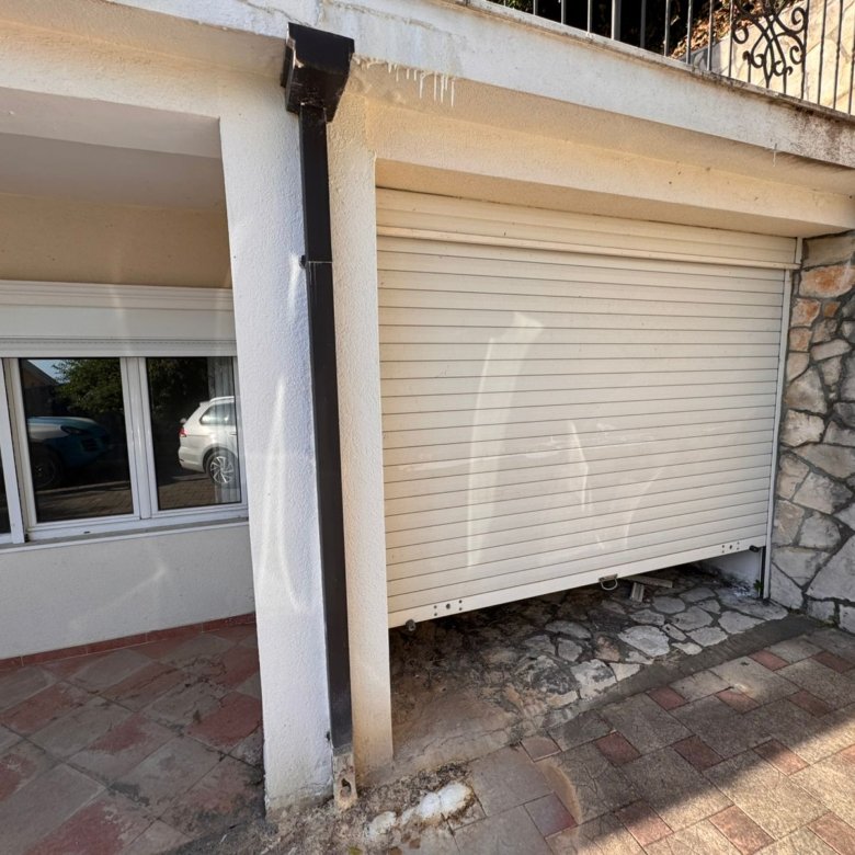 Modern stone and concrete garage with white roll-up door, tiled drive, and reflective windows&mdash;prime Ulcinj real estate by ekosphere doo.