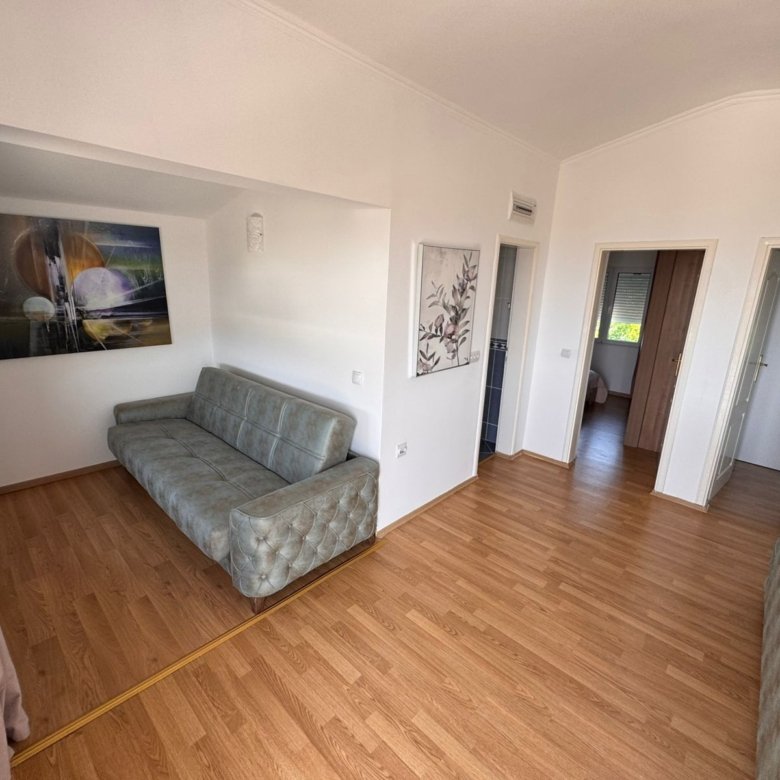 Modern Ulcinj property with light wood floors, sleek gray sofa, wall art, and open layout. Listed by immorenta.me, Ekosphere doo.