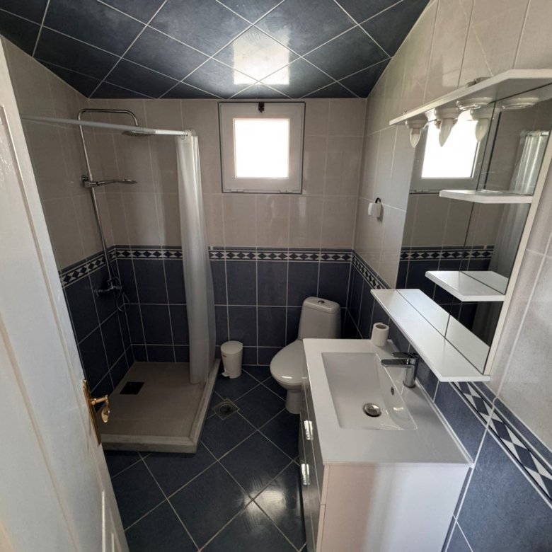 Modern Ulcinj Montenegro property bathroom: blue-white tiles, glass shower, window. Invest with immorenta.me by ekosphere doo.