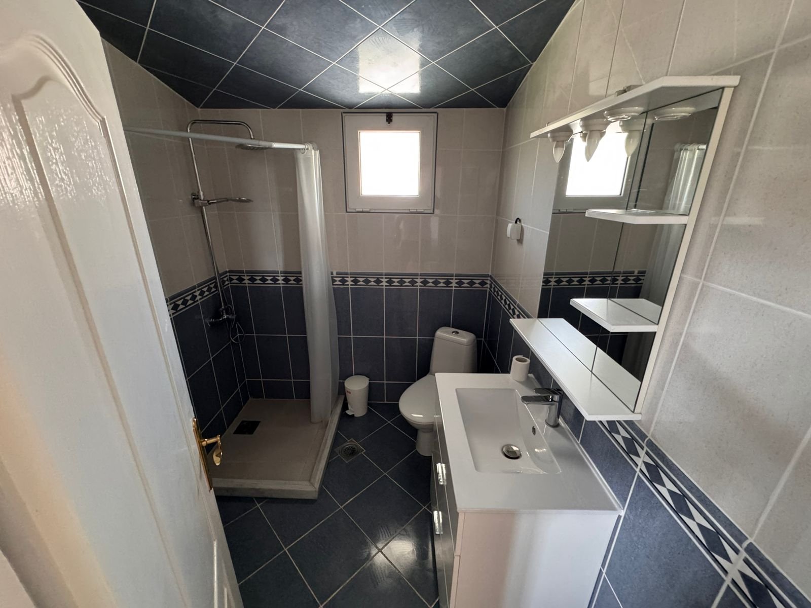 Modern Ulcinj Montenegro property bathroom: blue-white tiles, glass shower, window. Invest with immorenta.me by ekosphere doo.