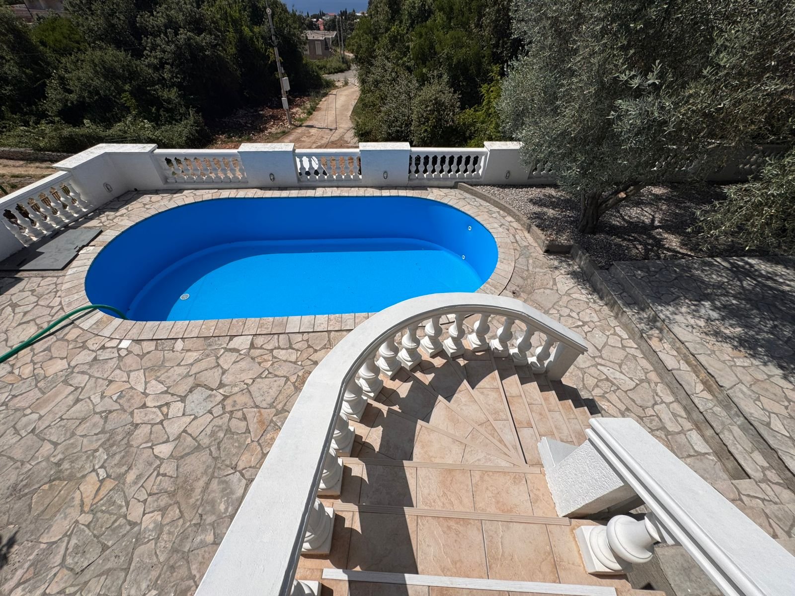 Elegant curved stone staircase with white railings to private pool, stone patio, and lush trees&mdash;prime Ulcinj real estate by ekosphere doo.