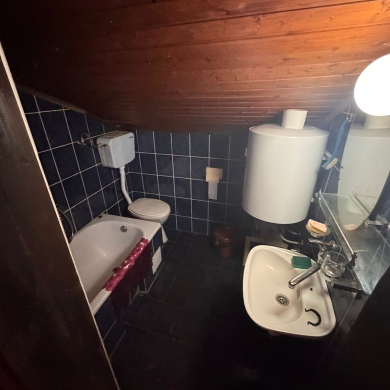 Modern bathroom in Ulcinj with blue tiles, wood-paneled ceiling, bathtub, and premium fixtures. Exclusive at immorenta.me/Ekosphere.