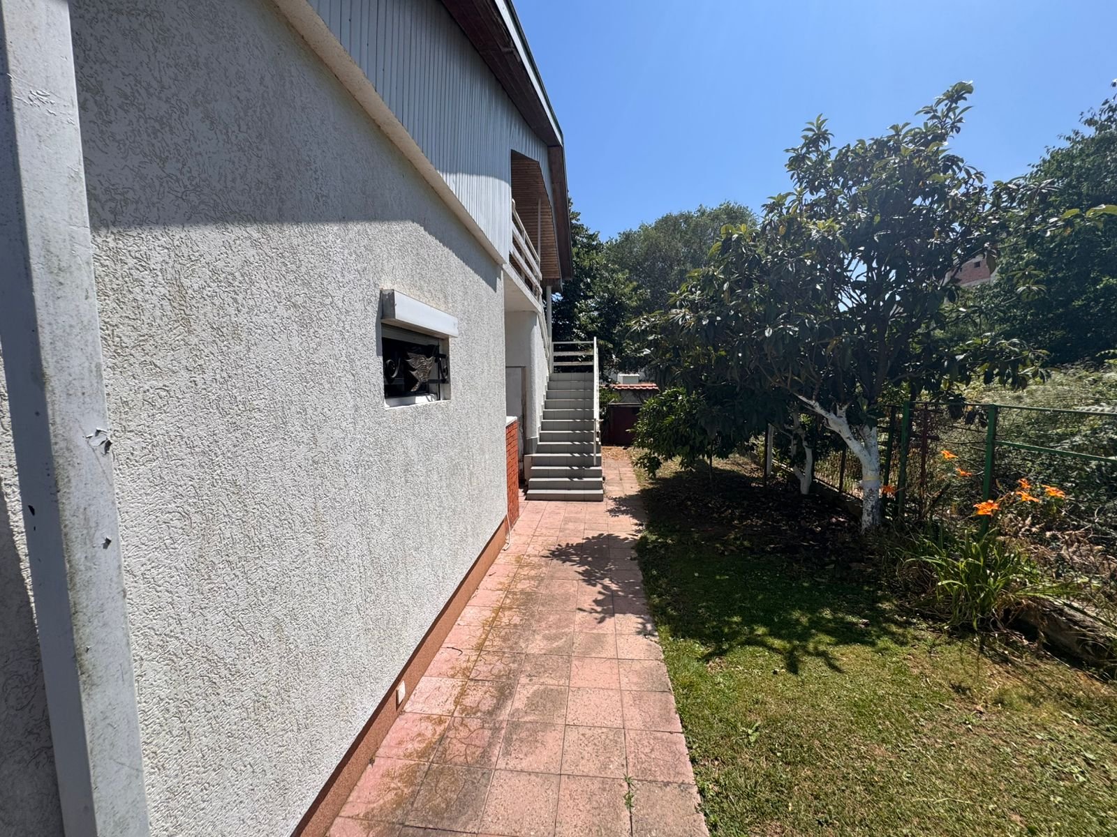 Stylish Ulcinj house with textured facade, lush garden, paved path, and stairs&mdash;ideal investment on immorenta.me by ekosphere doo.