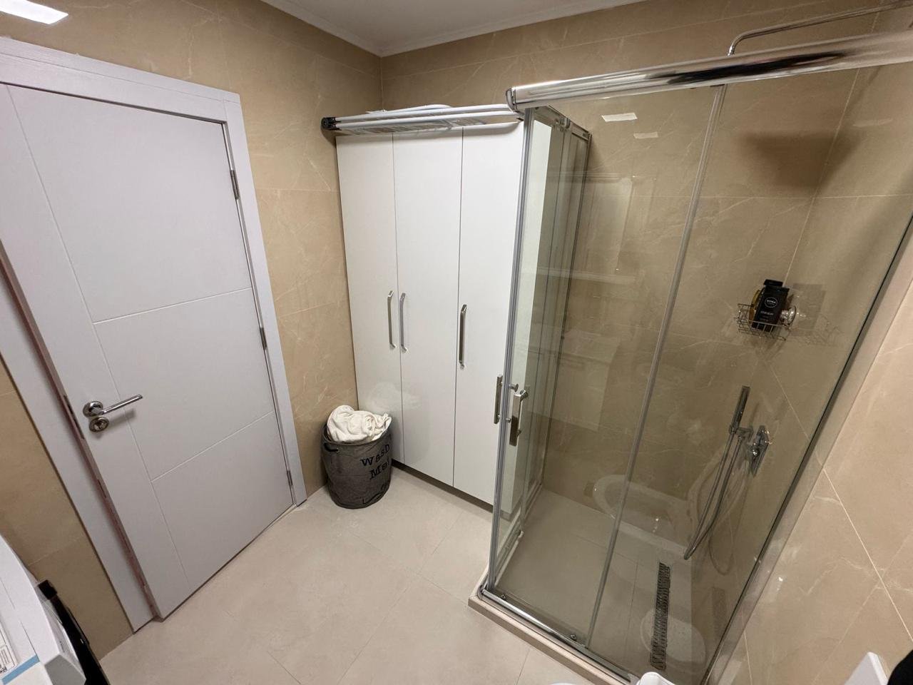 Elegant modern bathroom in Ulcinj, with beige tiles, glass shower, and storage; a premium investment by immorenta.me/Ekosphere doo.