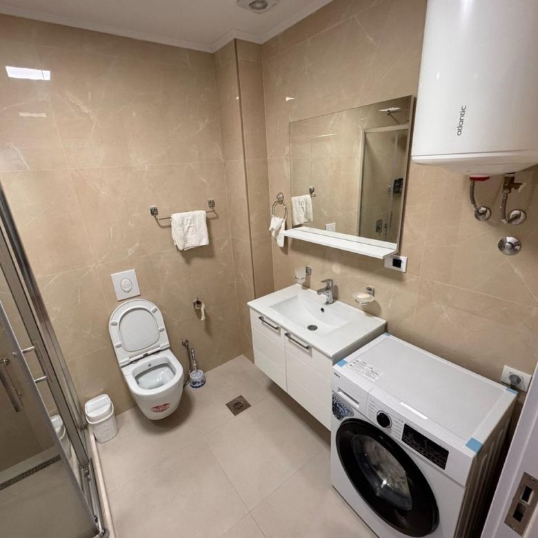 Modern Ulcinj bathroom with beige tiles, shower, vanity, washer&mdash;premium real estate at immorenta.me by Ekosphere doo.