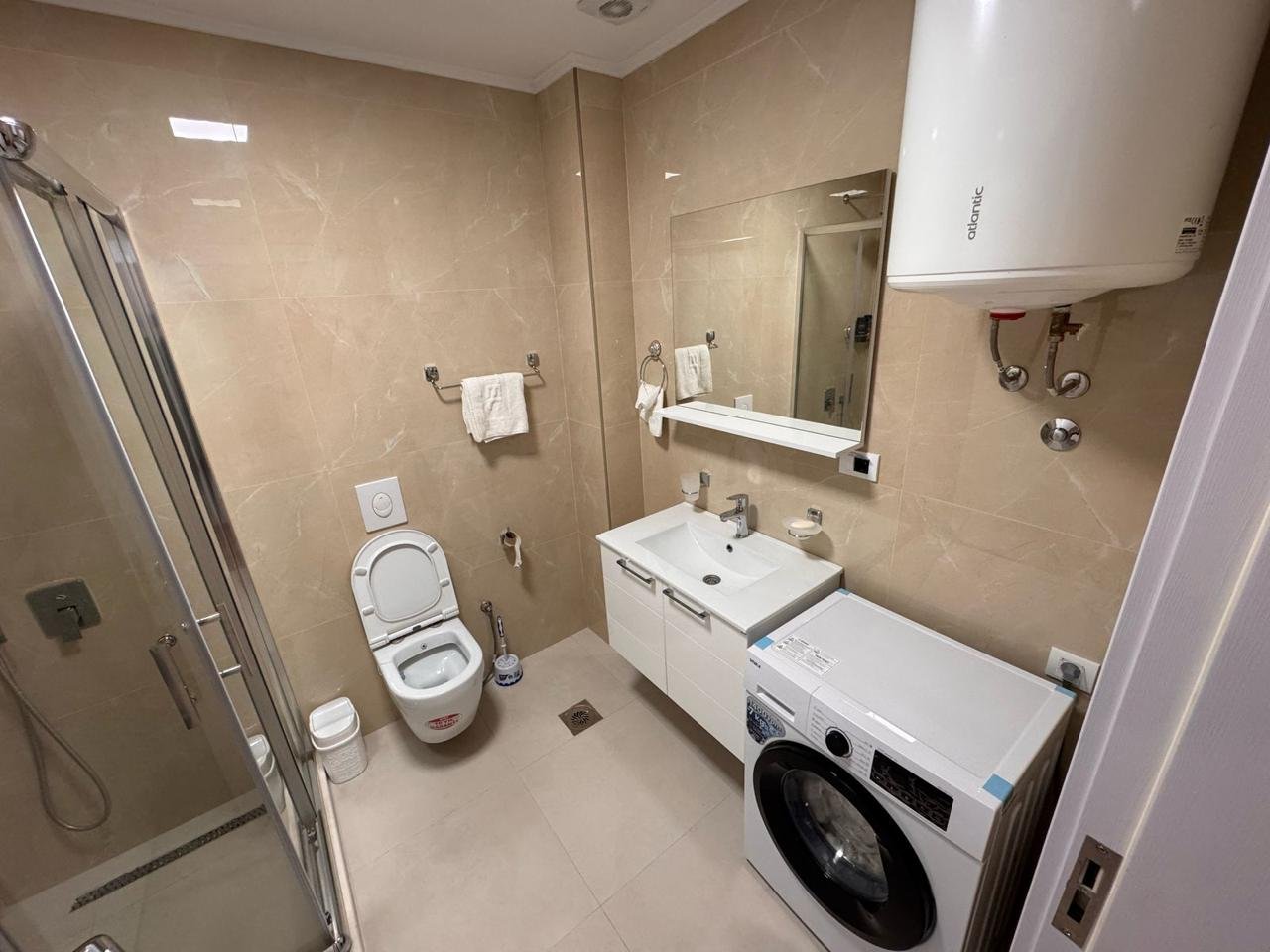 Modern Ulcinj bathroom with beige tiles, shower, vanity, washer&mdash;premium real estate at immorenta.me by Ekosphere doo.