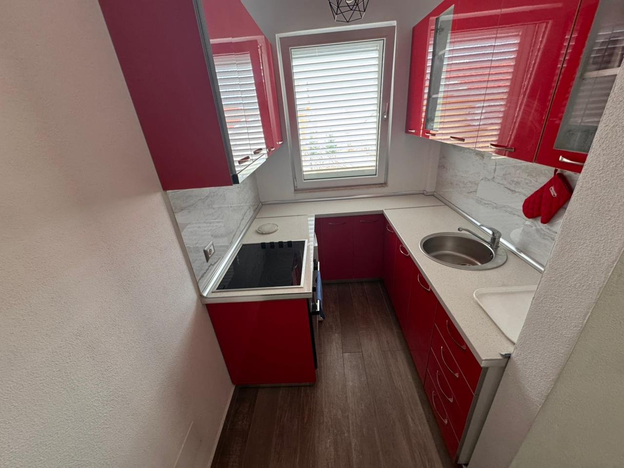 Modern Ulcinj kitchen: red cabinets, white countertop, electric stovetop. Ideal investment. Listed by immorenta.me, Ekosphere Doo.