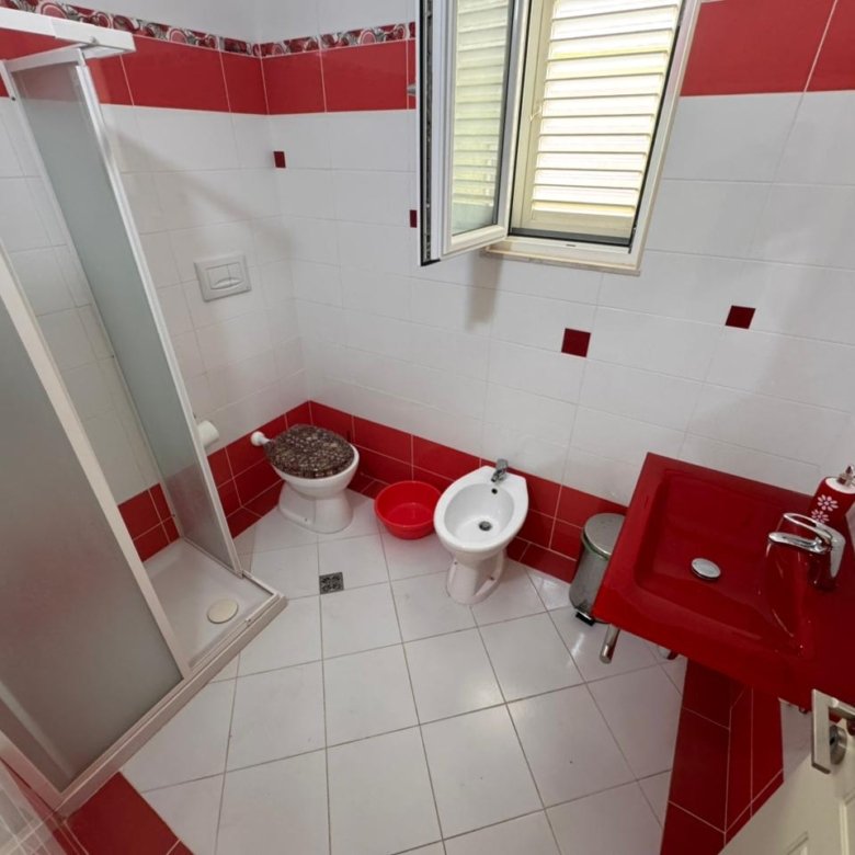 Modern bathroom in Ulcinj property: white/red tiles, shower, bidet, red sink. Invest via immorenta.me by ekosphere doo.