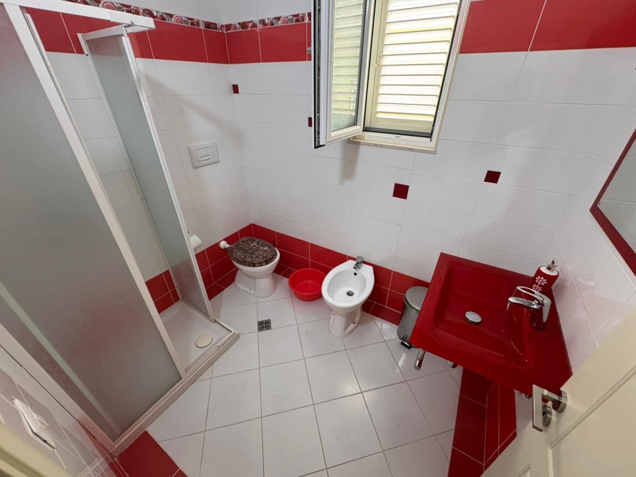 Modern bathroom in Ulcinj property: white/red tiles, shower, bidet, red sink. Invest via immorenta.me by ekosphere doo.