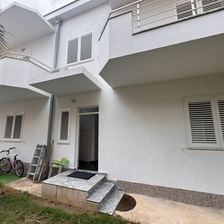 Modern white two-story home in Ulcinj, with porch, open entry, child-friendly lawn by palm tree. Listed on immorenta.me by ekosphere doo.