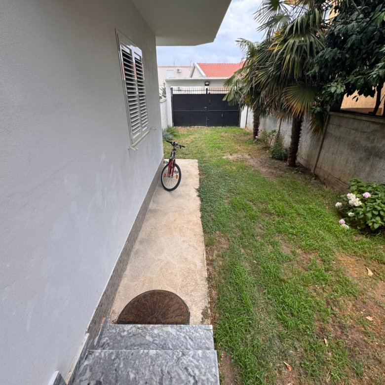 Modern Ulcinj property for sale&mdash;white house, lush plants, private path to secure gate. Invest via immorenta.me by ekosphere doo.