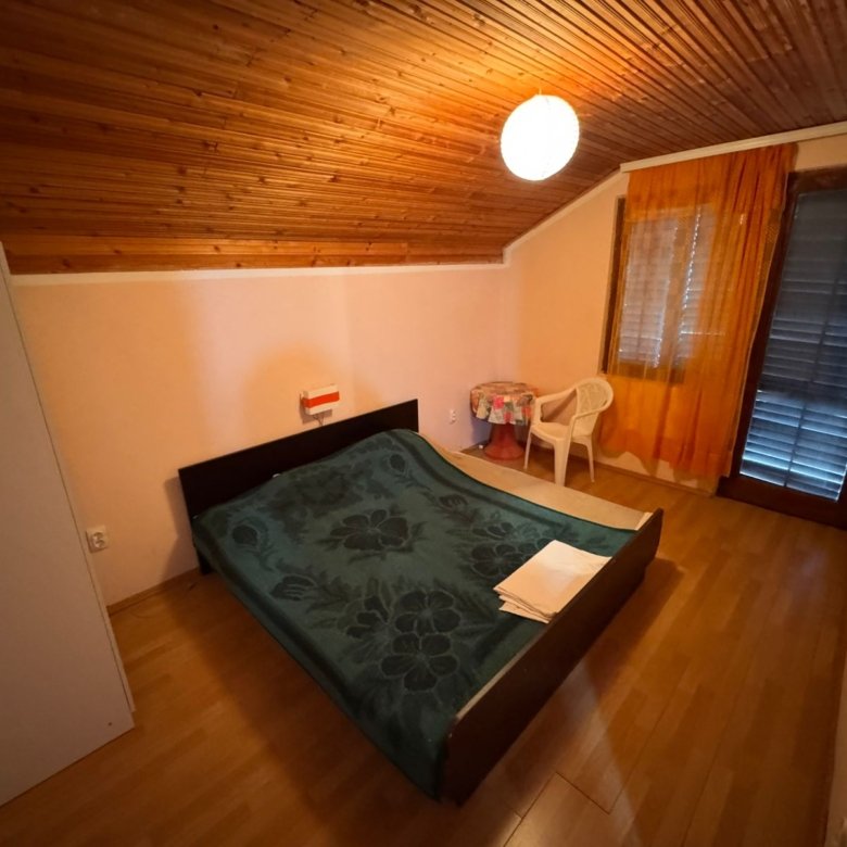 Inviting Ulcinj bedroom with sloped wood ceiling, double bed, orange curtains&mdash;ideal Montenegro investment. Listed on immorenta.me by Ekosphere doo.