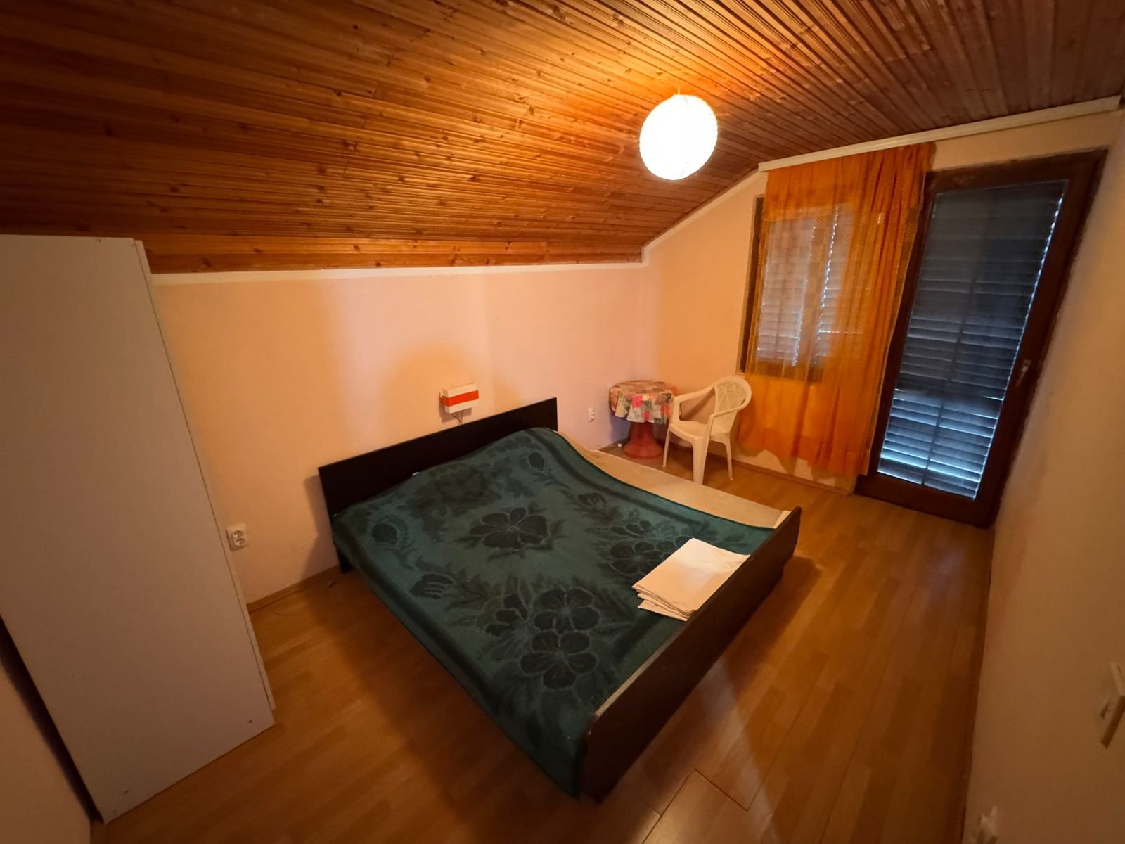 Inviting Ulcinj bedroom with sloped wood ceiling, double bed, orange curtains&mdash;ideal Montenegro investment. Listed on immorenta.me by Ekosphere doo.