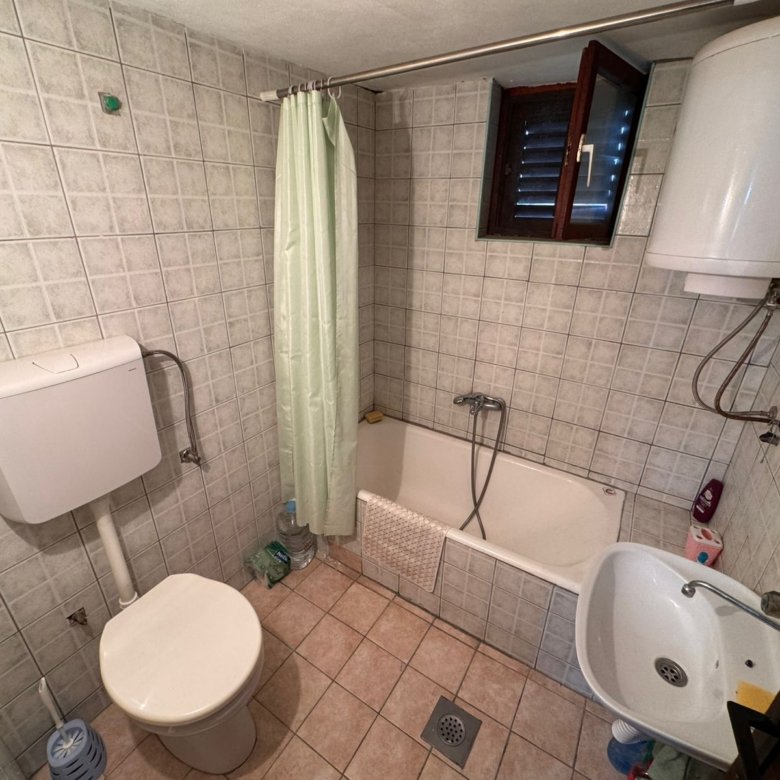 Modern tiled bathroom in Ulcinj property: toilet, eco water heater, tub with shower, sink, window&mdash;exclusive at immorenta.me.