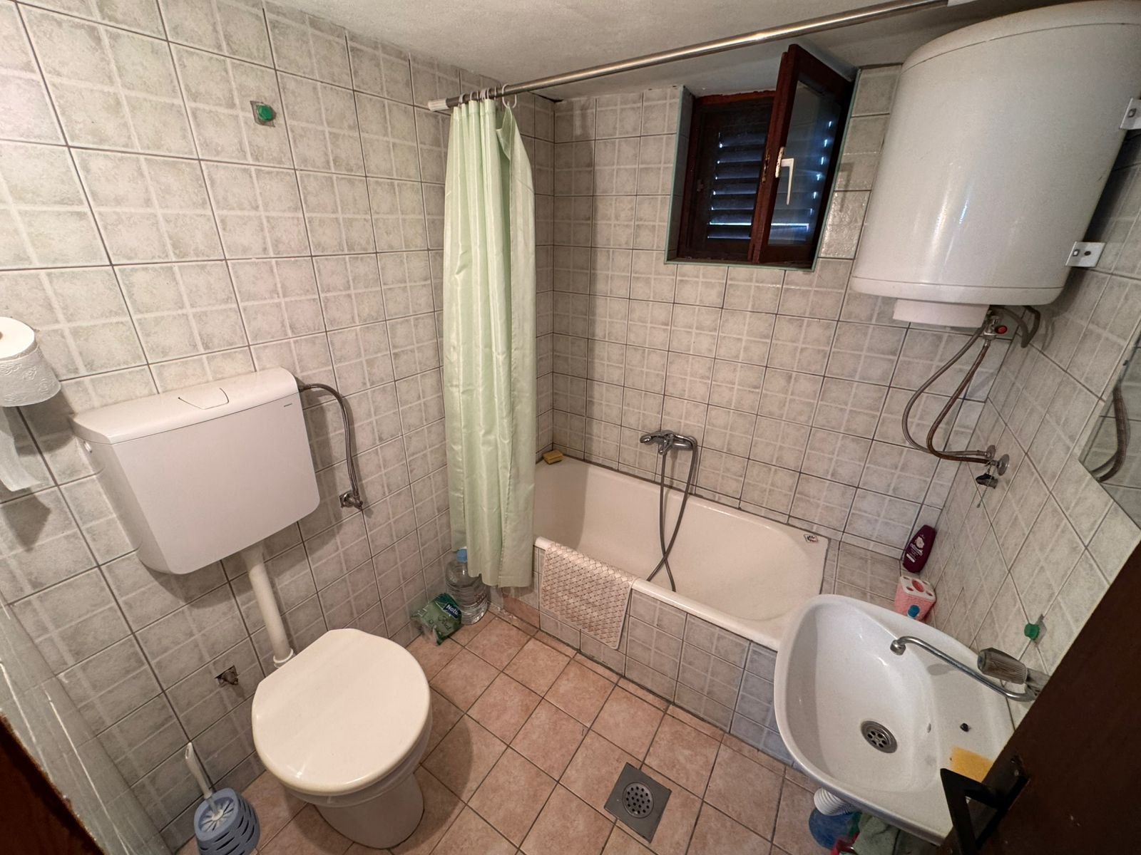 Modern tiled bathroom in Ulcinj property: toilet, eco water heater, tub with shower, sink, window&mdash;exclusive at immorenta.me.