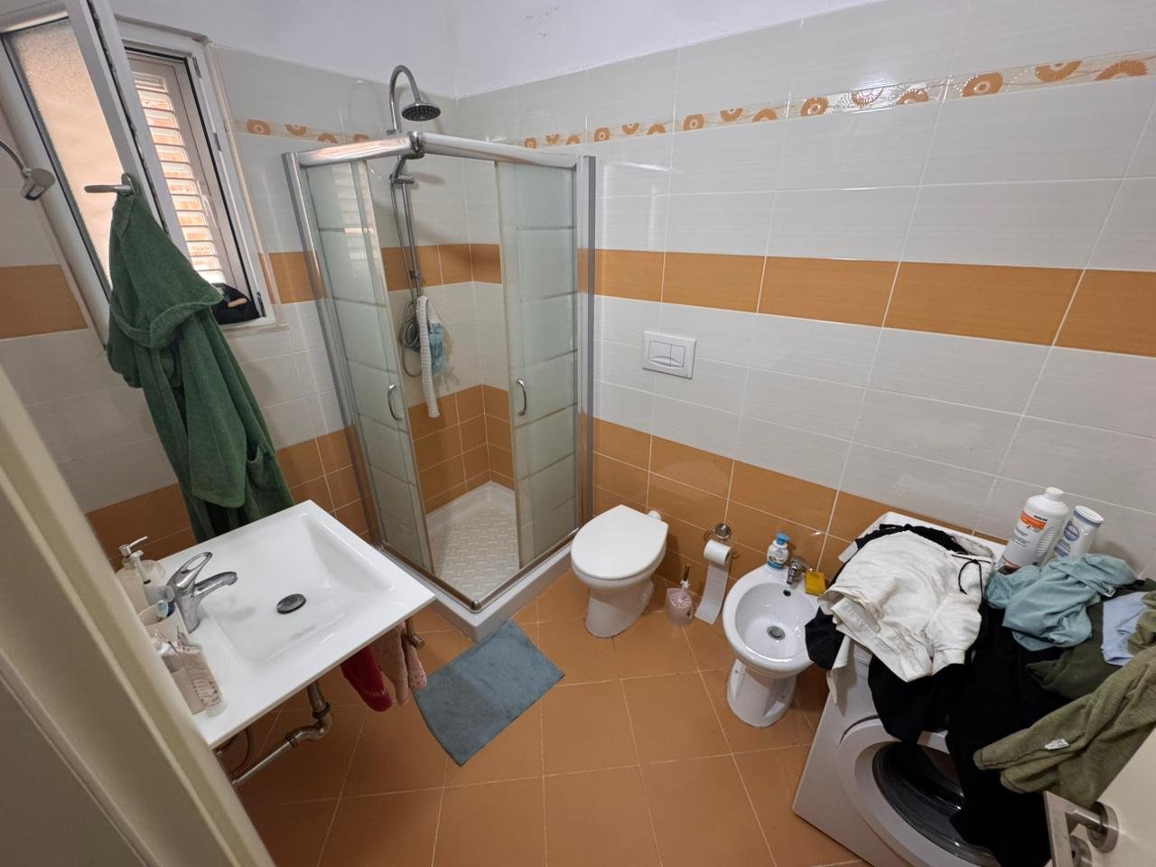 Modern bathroom in Ulcinj property with glass shower, bidet, washer, and orange tiles. Exclusive listing by ekosphere doo on immorenta.me.