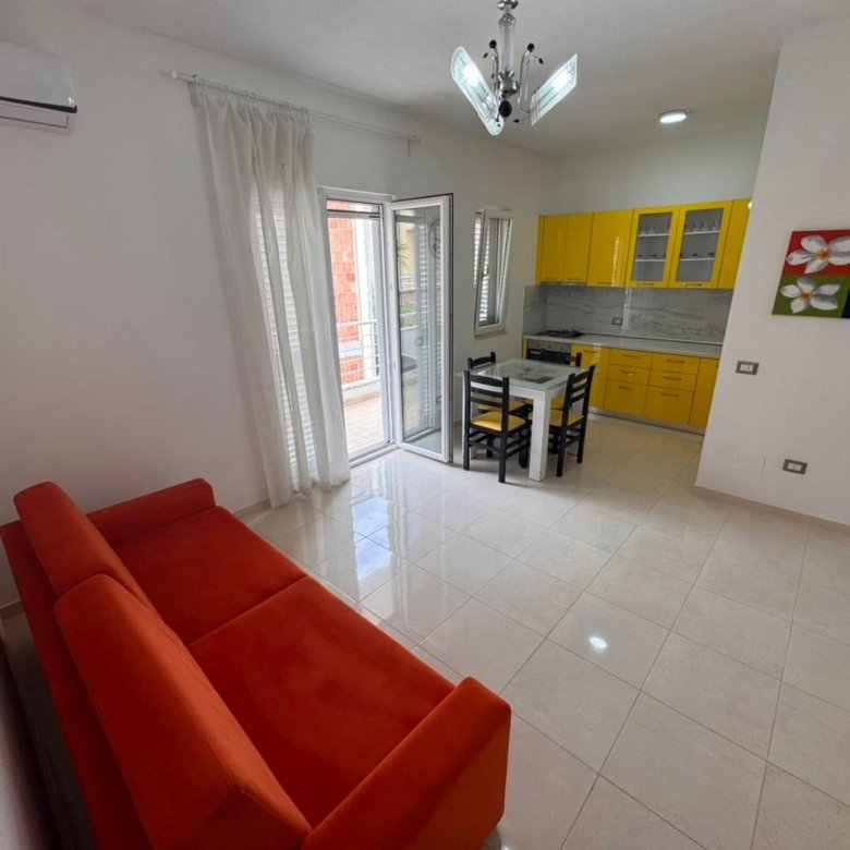 Modern Ulcinj apartment with red-orange sofa, yellow kitchen, and balcony. Prime investment via immorenta.me by ekosphere doo.