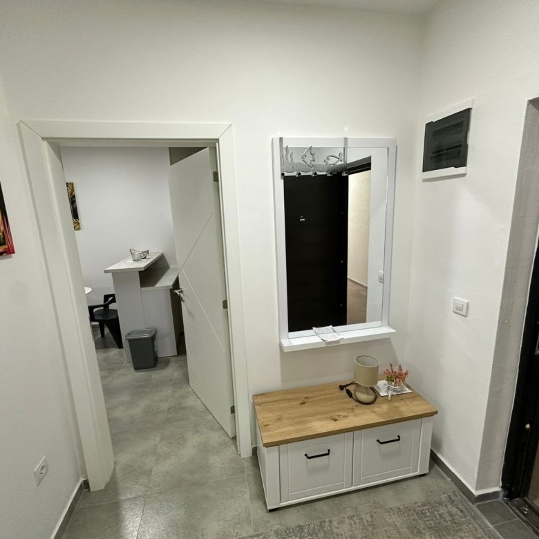 Modern hallway in Ulcinj property: gray tile floors, white walls, vanity, plant, and intercom. Montenegro-listings.me by Ekosphere.