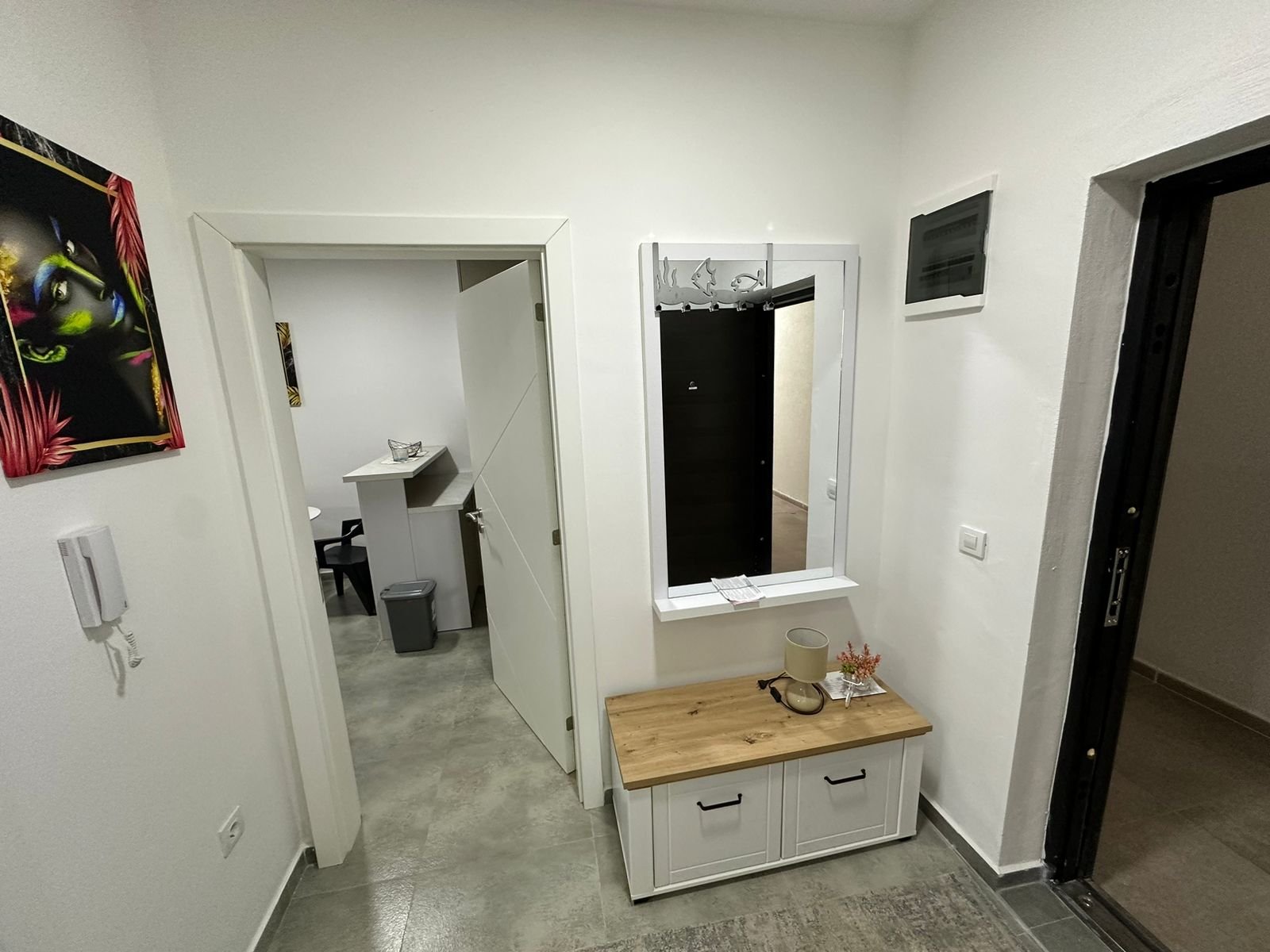 Modern hallway in Ulcinj property: gray tile floors, white walls, vanity, plant, and intercom. Montenegro-listings.me by Ekosphere.
