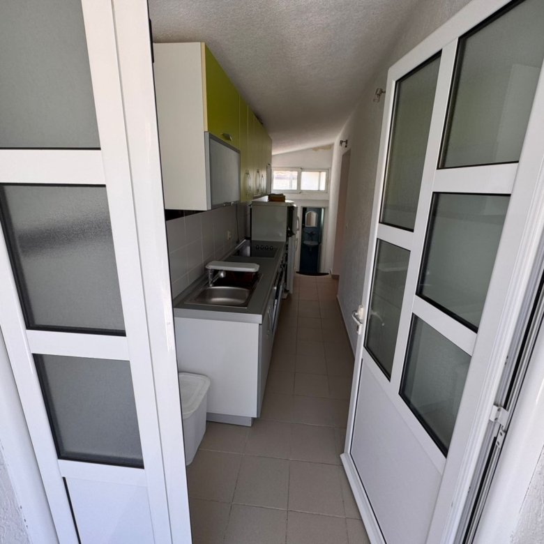 Modern narrow kitchen in Ulcinj property: sleek white cabinets, green accent, appliances, ideal Montenegro investment. By ekosphere doo.